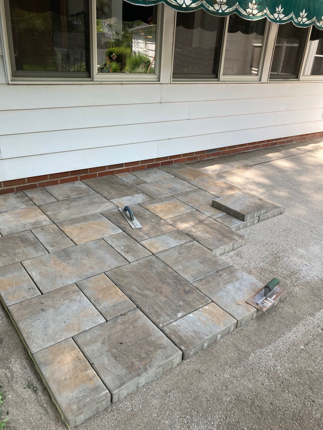 Stone patio with uneven pavers and exposed utility openings beside a house exterior