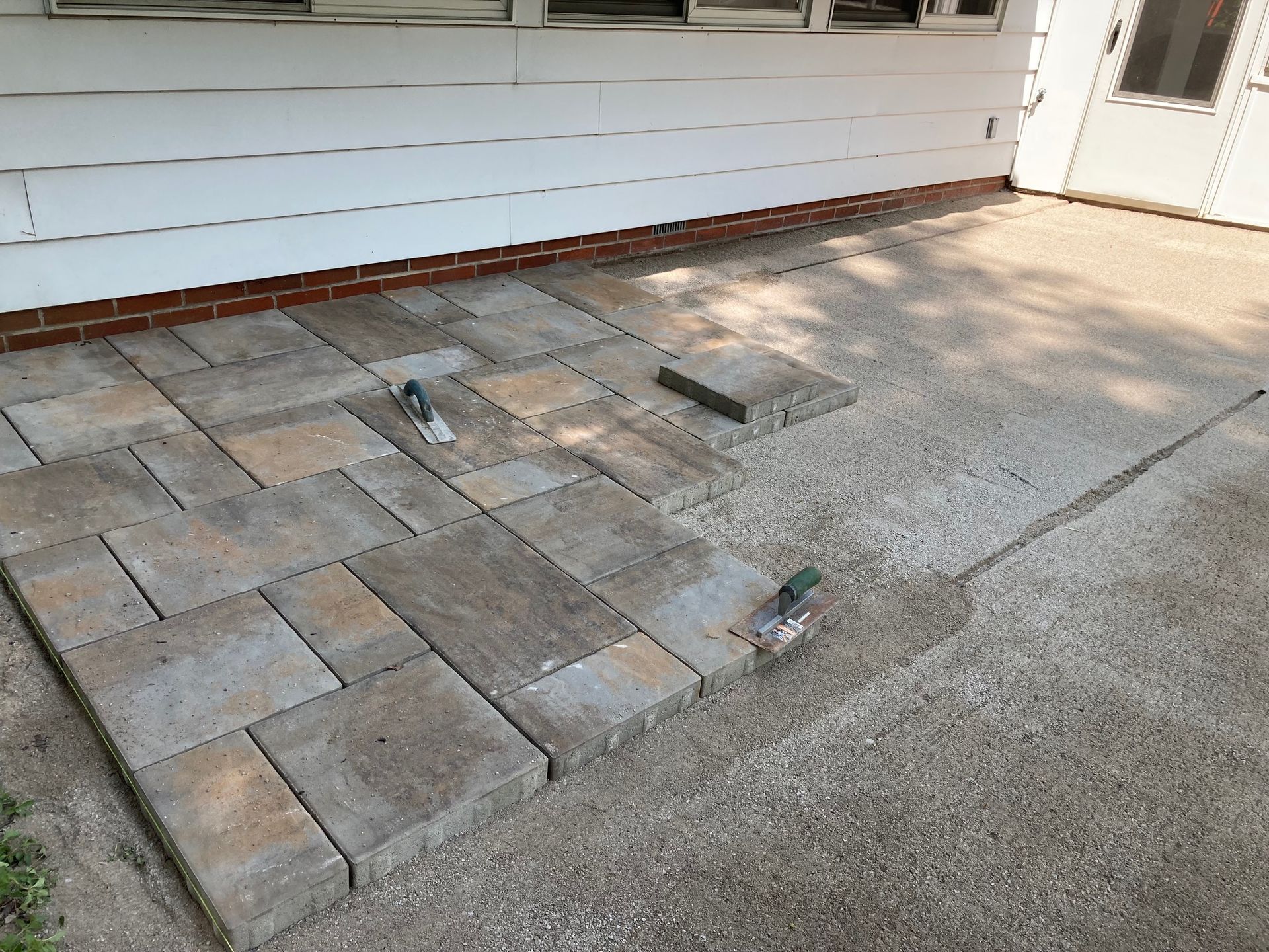 Broken concrete patio with uneven pavers beside a house wall and door.
