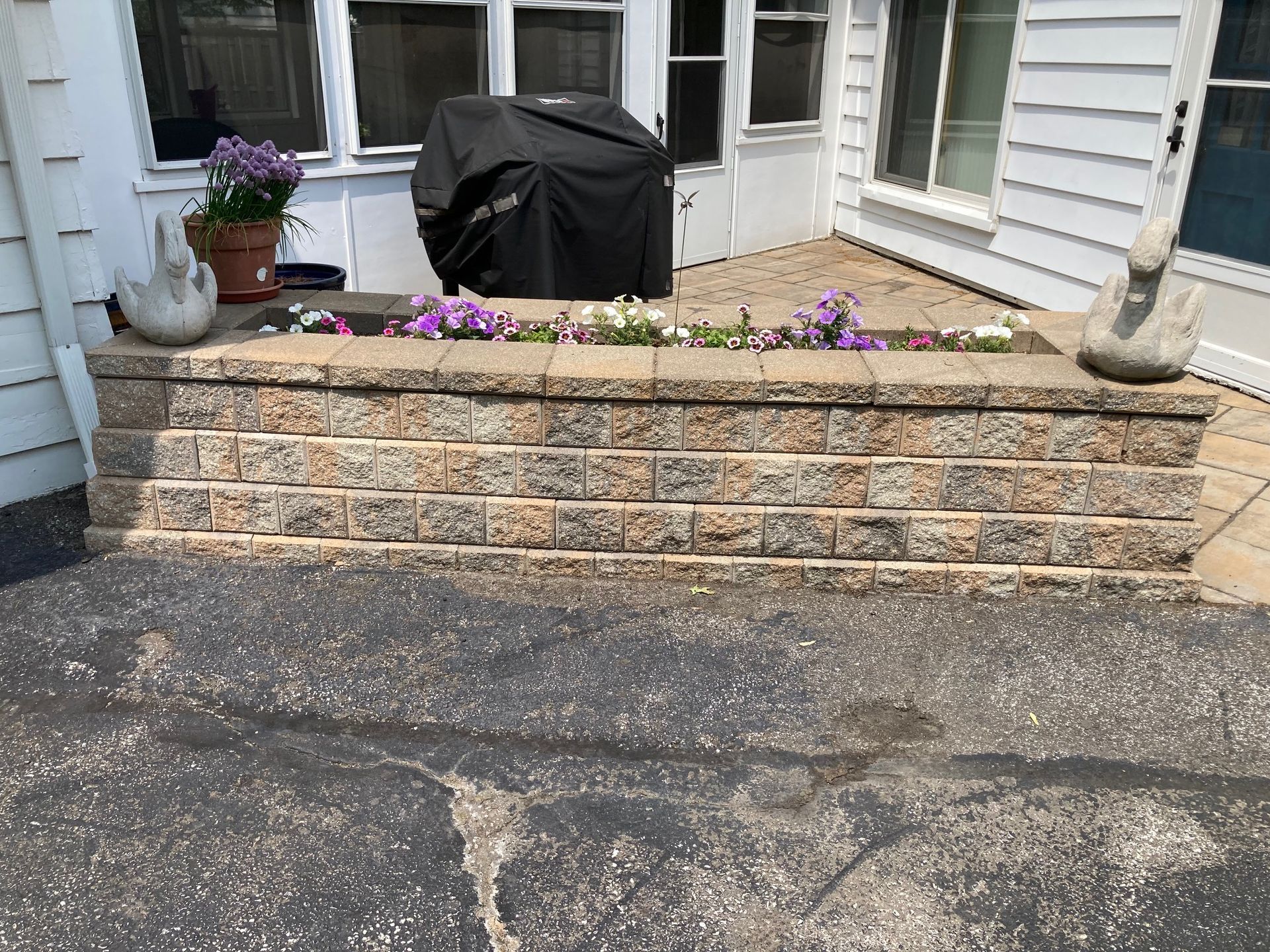 Front stoop with stone planter wall, purple flowers, and a covered grill on a porch.