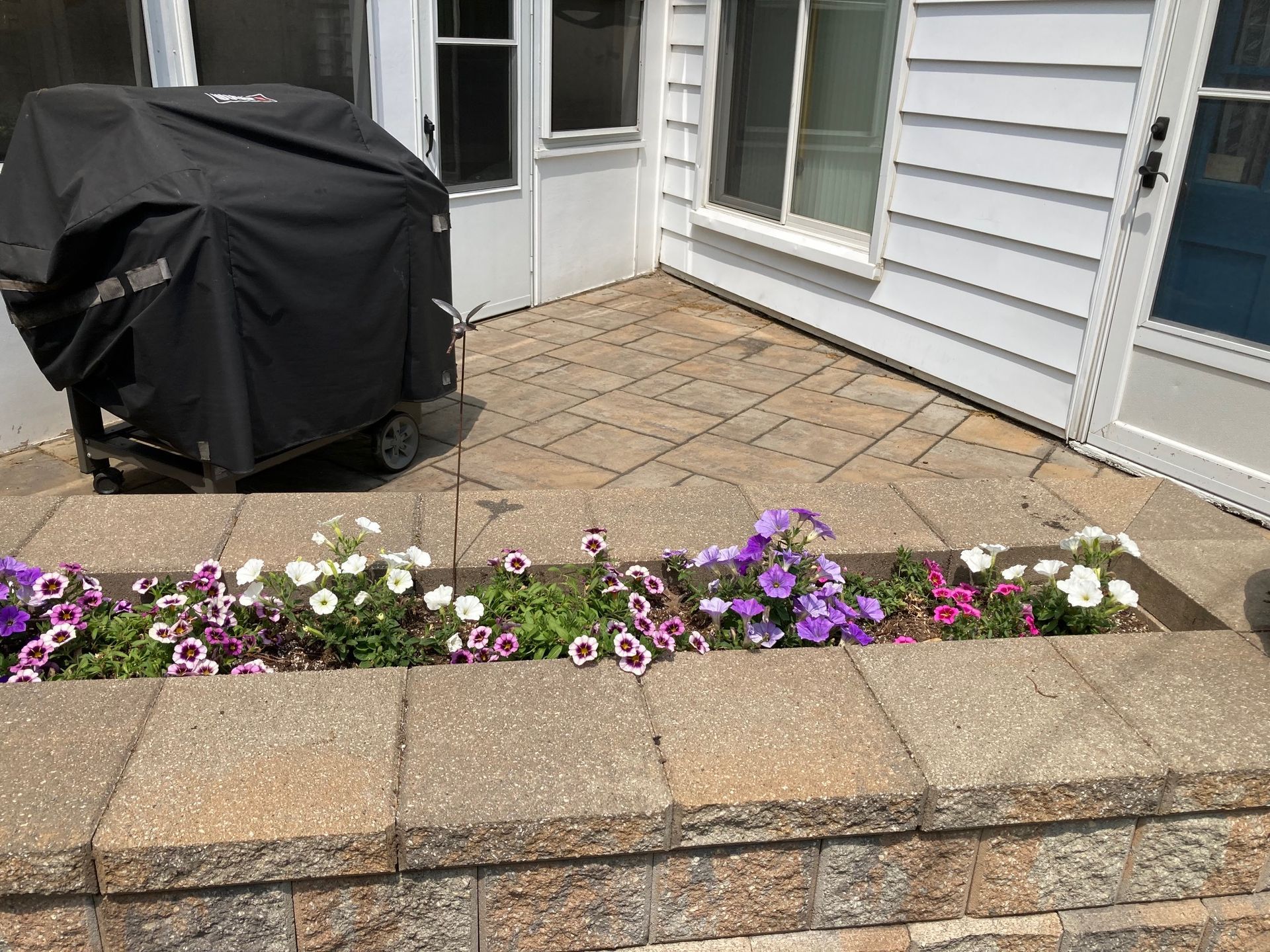 Back patio with a covered grill, stone pavers, and a narrow flower bed of pink and white blossoms