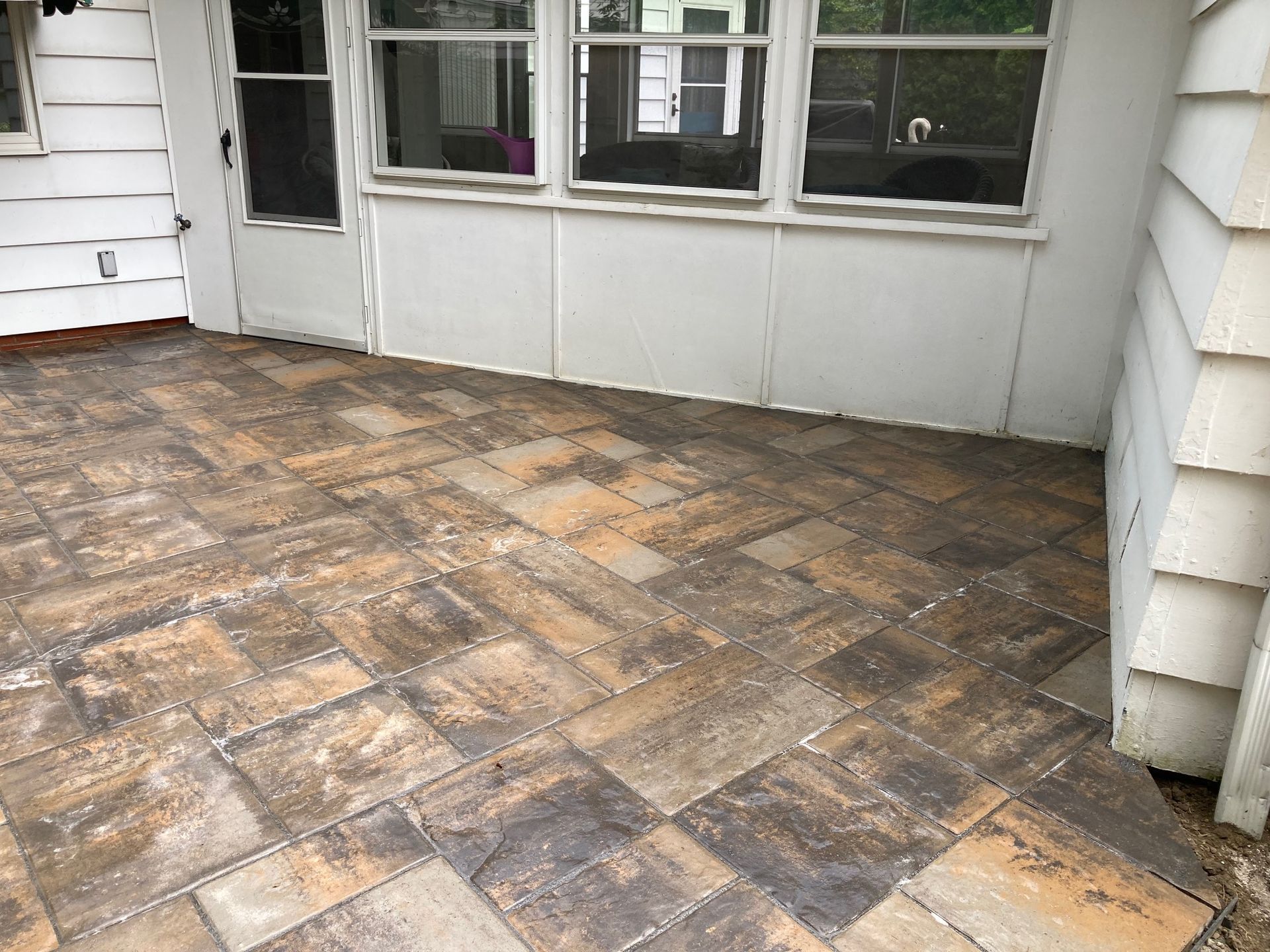 Weathered brick patio outside a house with white siding and windows