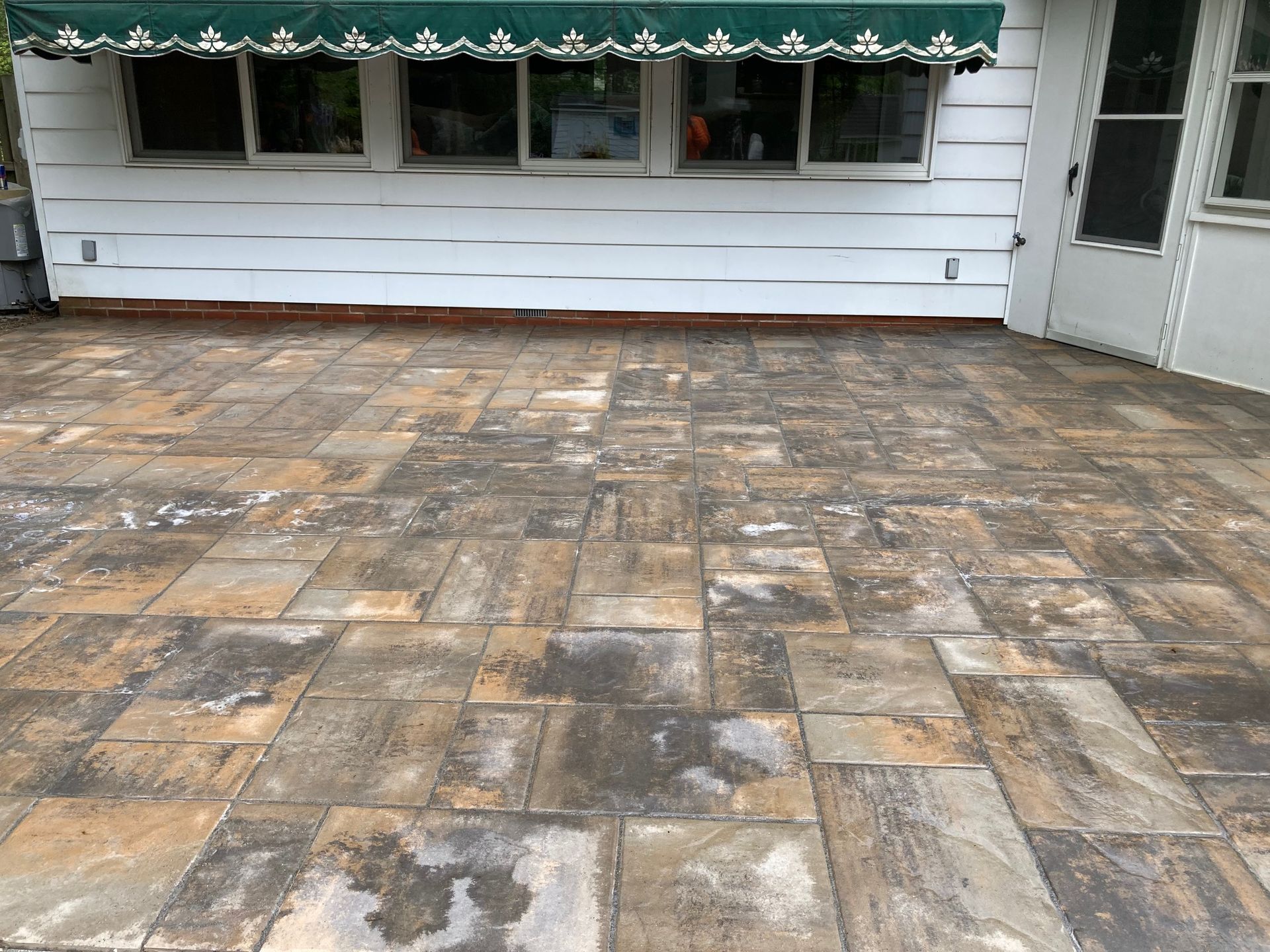 Patio with multicolored stone pavers in front of a white house with windows and a green awning