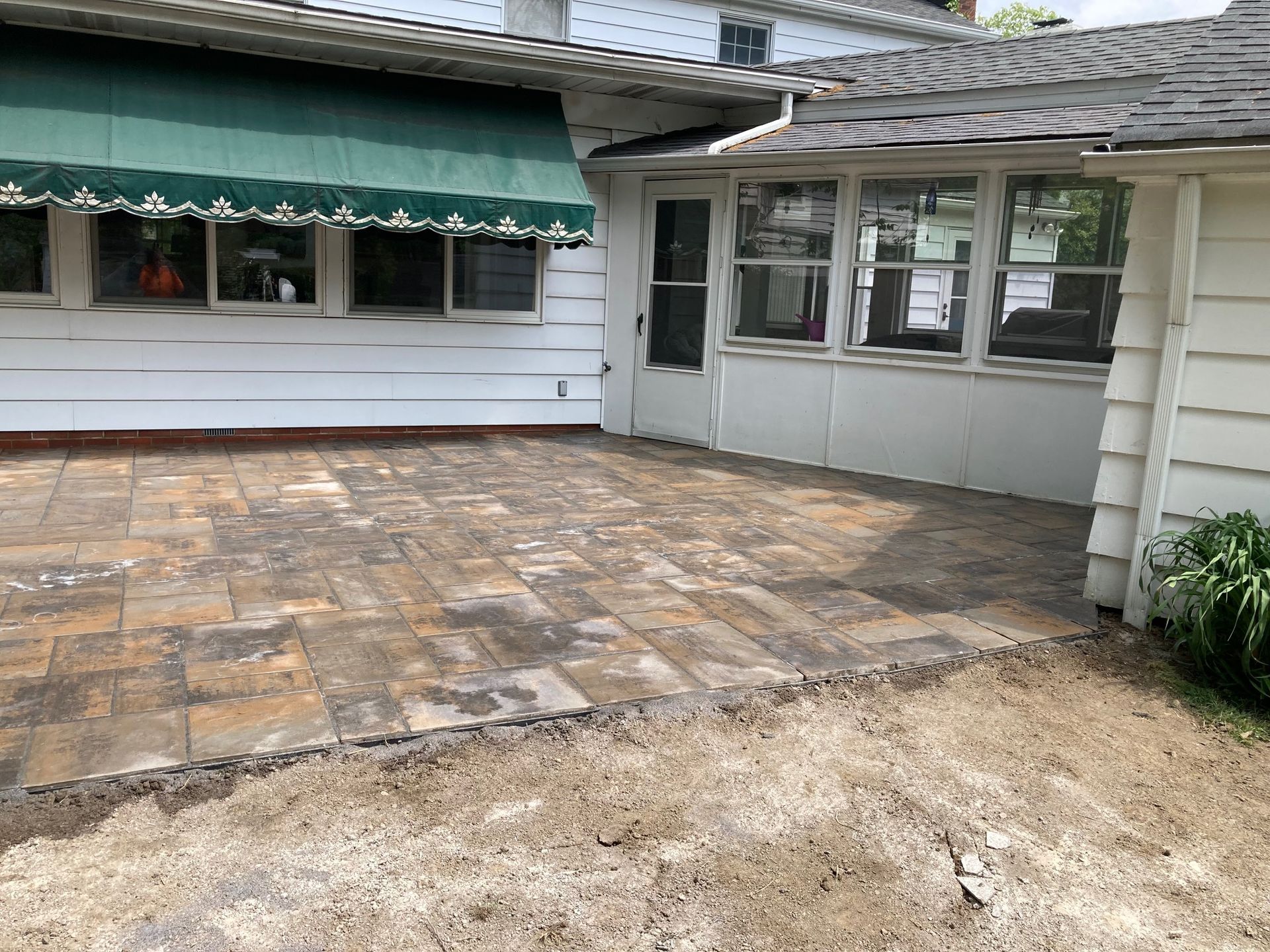 Patio with stone pavers beside a white house and screened porch under a green awning