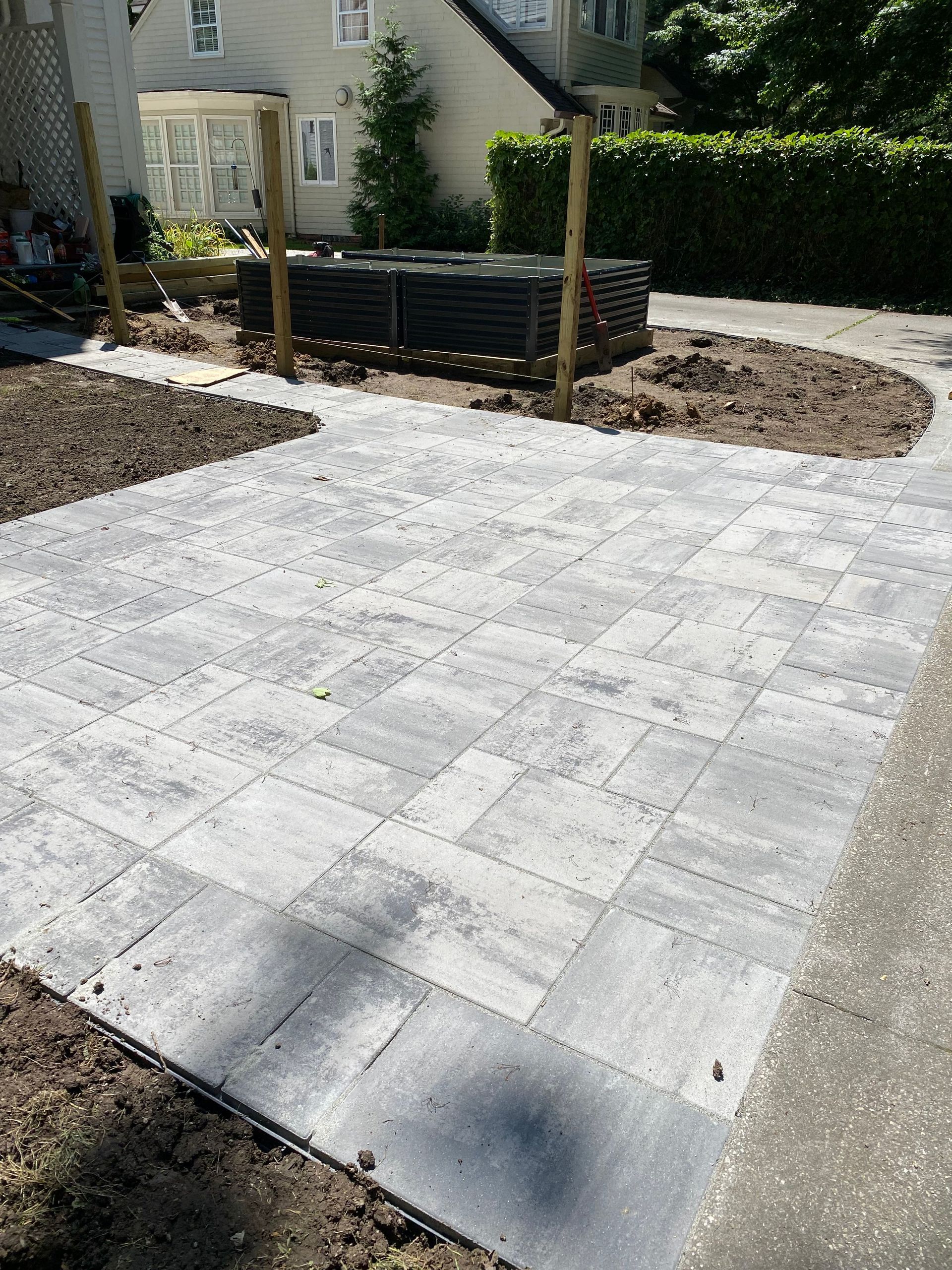 Freshly paved light-gray stone patio in a landscaped backyard with garden beds and a fence