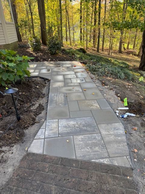 Stone walkway leading through a wooded backyard with pavers, mulch, and a short stair landing