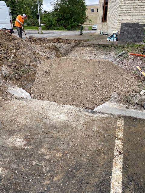 Roadwork site with a worker in orange vest beside a large gravel-filled trench