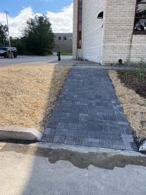 Brick walkway leading from a sidewalk to a building entrance beside a grassy yard.