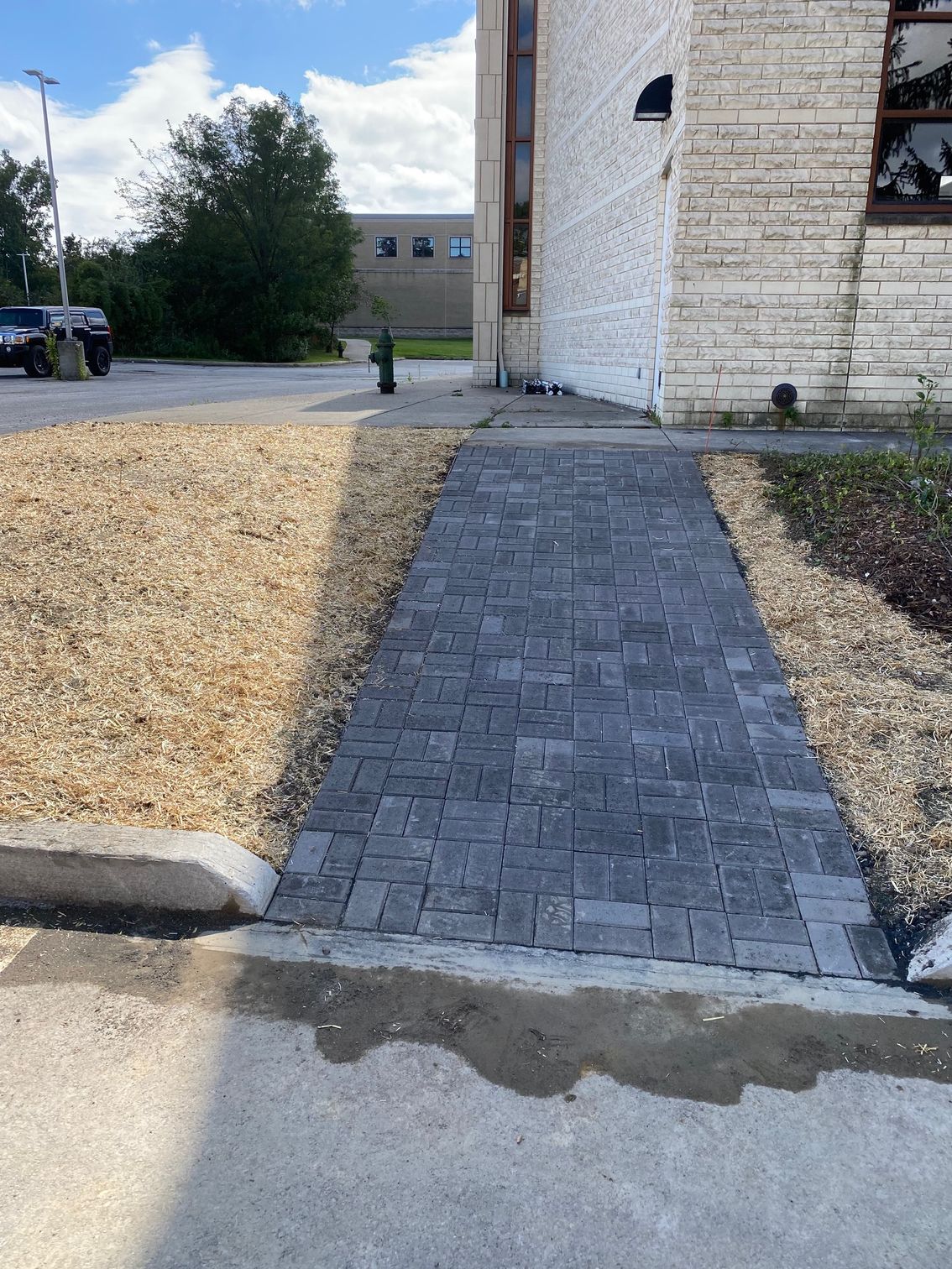 Brick walkway leading to a building entrance beside a gravel lot and white wall
