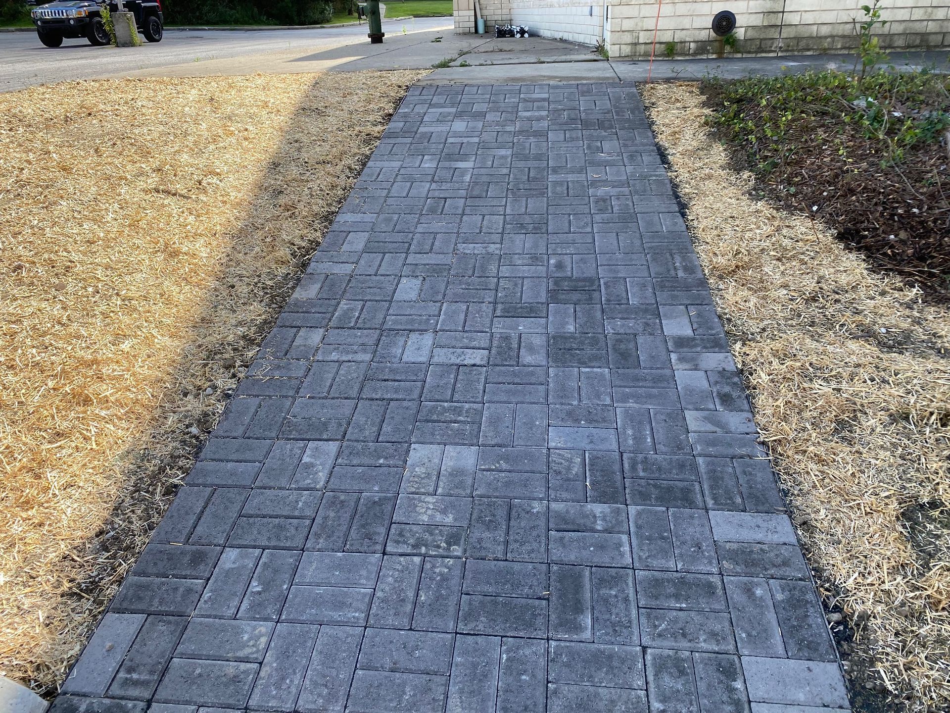 Gray brick walkway curving through a landscaped yard with dry grass on both sides