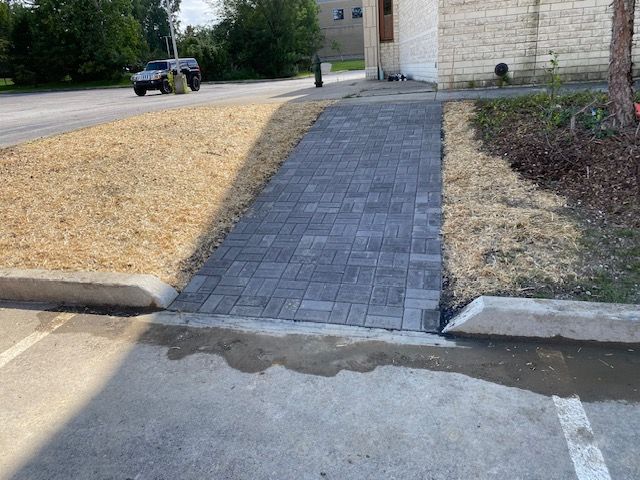 Brick sidewalk ramp between curb cuts leading from street to building entrance, with a parked car nearby.