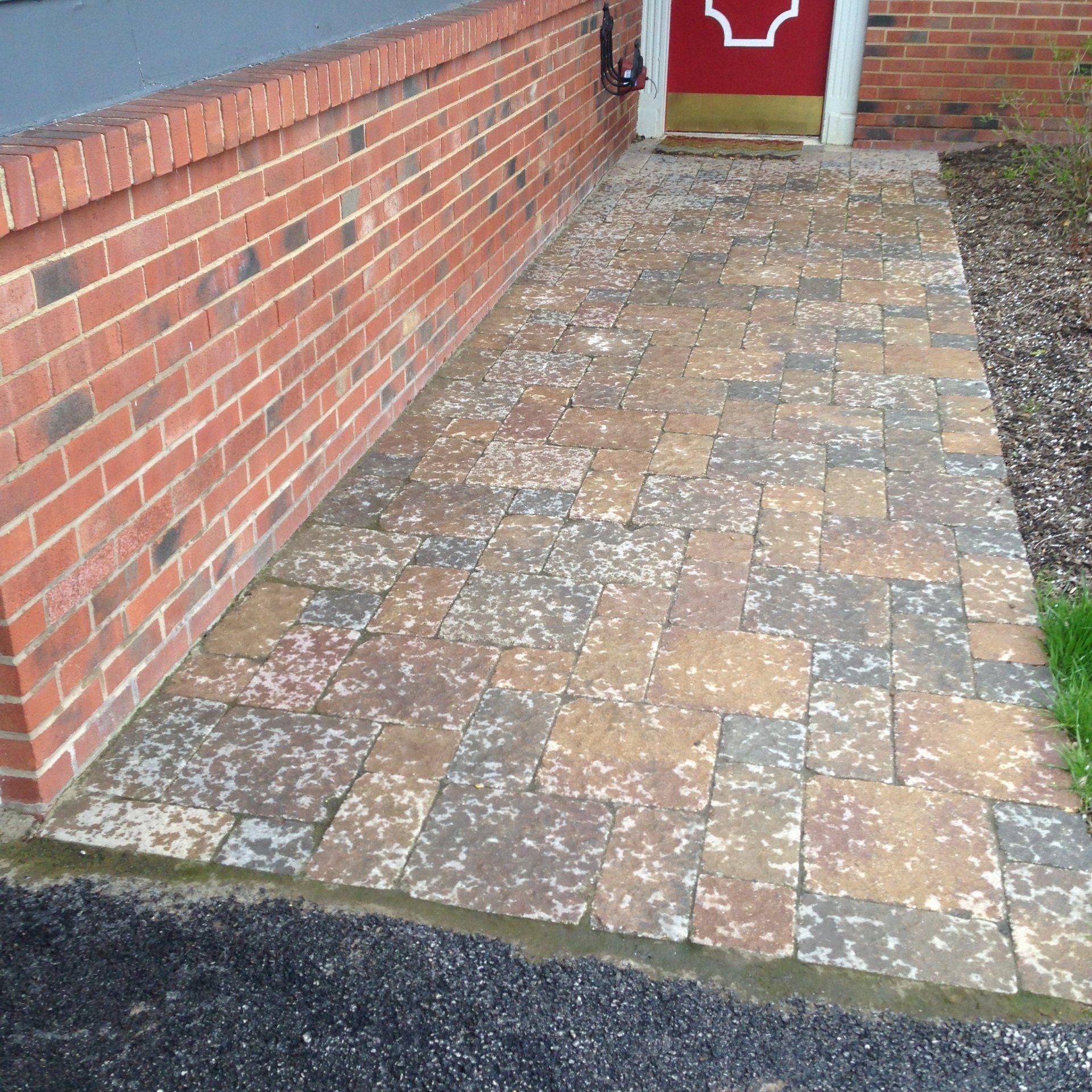 Brick wall beside a paved walkway leading to a red door