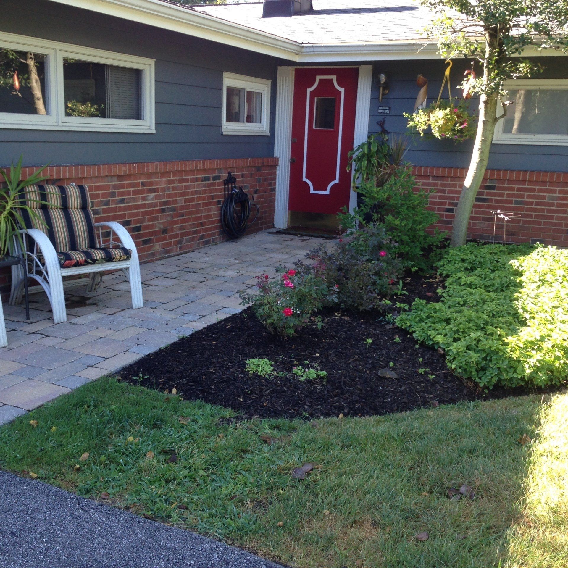 Front yard with red front door, brick house, patio chairs, and landscaped flower bed.