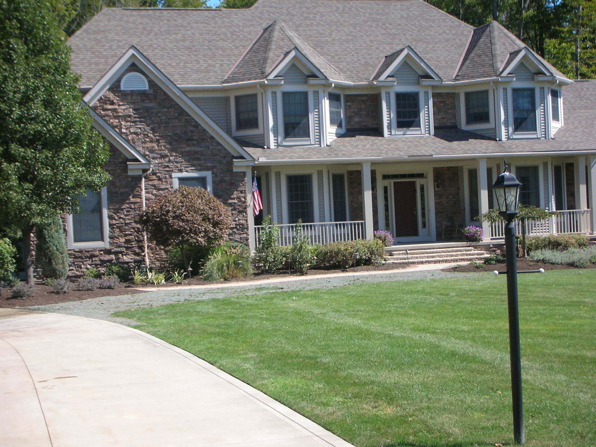Large brick suburban house with white porch, manicured lawn, and driveway in front