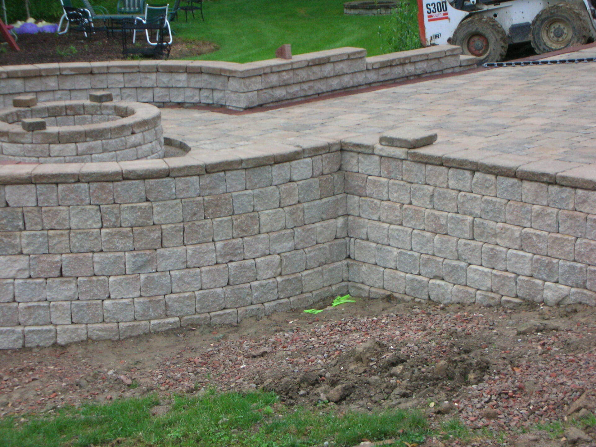 Stone retaining wall and steps in a landscaped outdoor area with grass and a paved path.