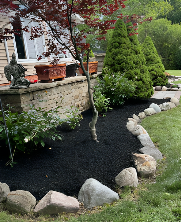 Front yard landscape with black mulch, stone border, shrubs, and a small tree by a house porch