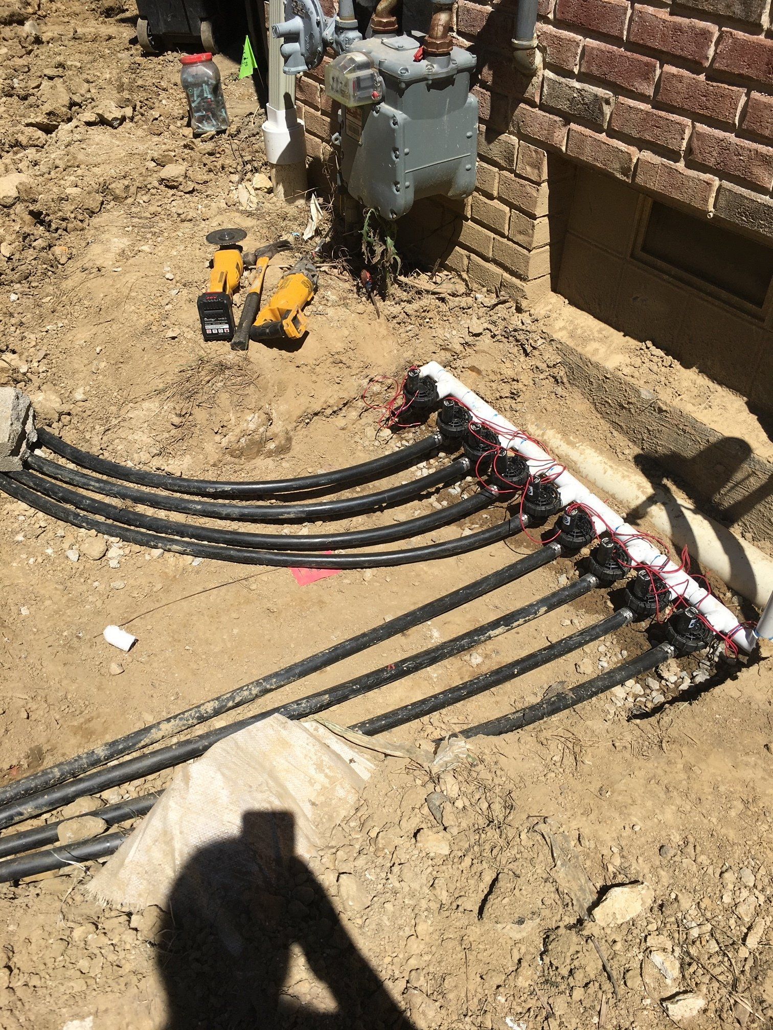 Construction worker installing underground cables beside a brick wall and utility box.