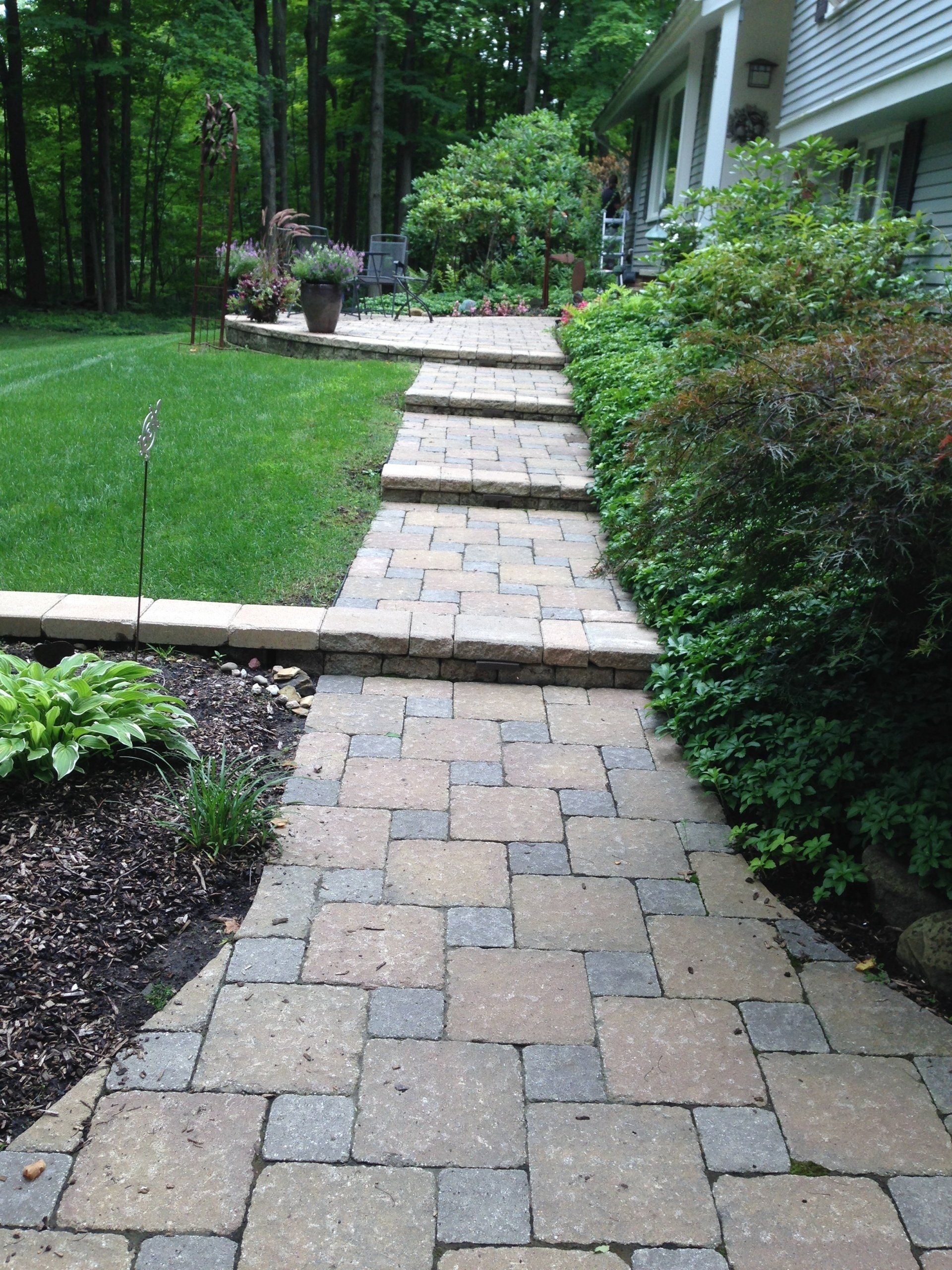 Brick garden walkway with steps leading through a landscaped yard beside a house and trees