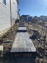 New concrete walkway beside a house, with steps leading toward a backyard and neighboring homes.