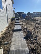 New stone walkway beside a house, with steps leading to a row of homes in the distance.