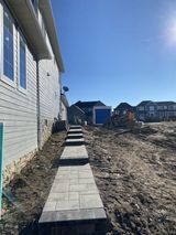 A concrete walkway beside a house in a new residential neighborhood under a clear blue sky.