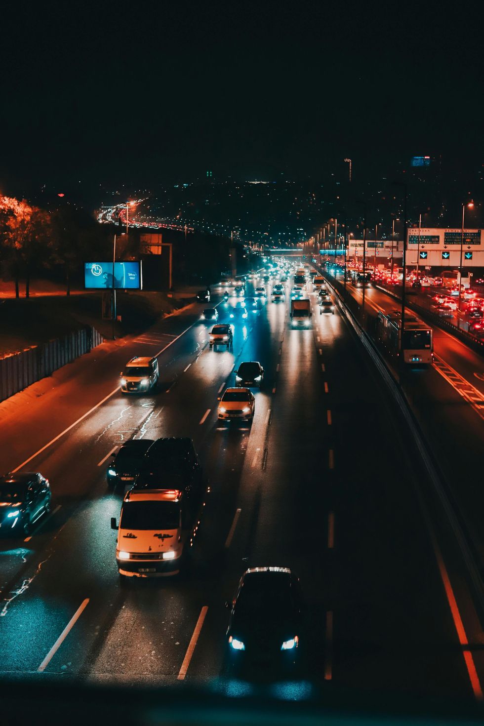 Night highway traffic with blurred headlights and taillights on a wet road, city lights in the distance
