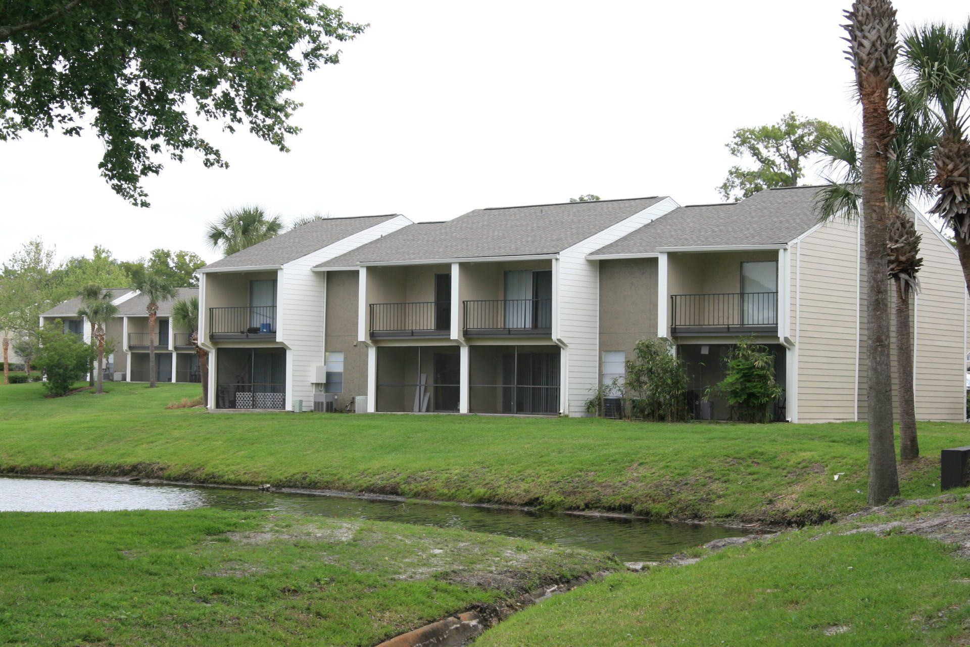 Apartment buildings beside a grassy canal under cloudy skies