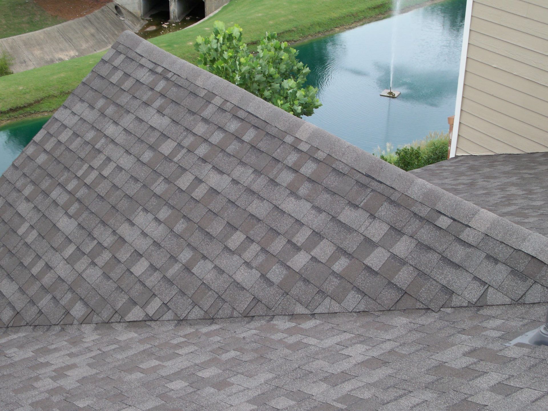Gray shingled roof beside a backyard pond with a fountain and green lawn
