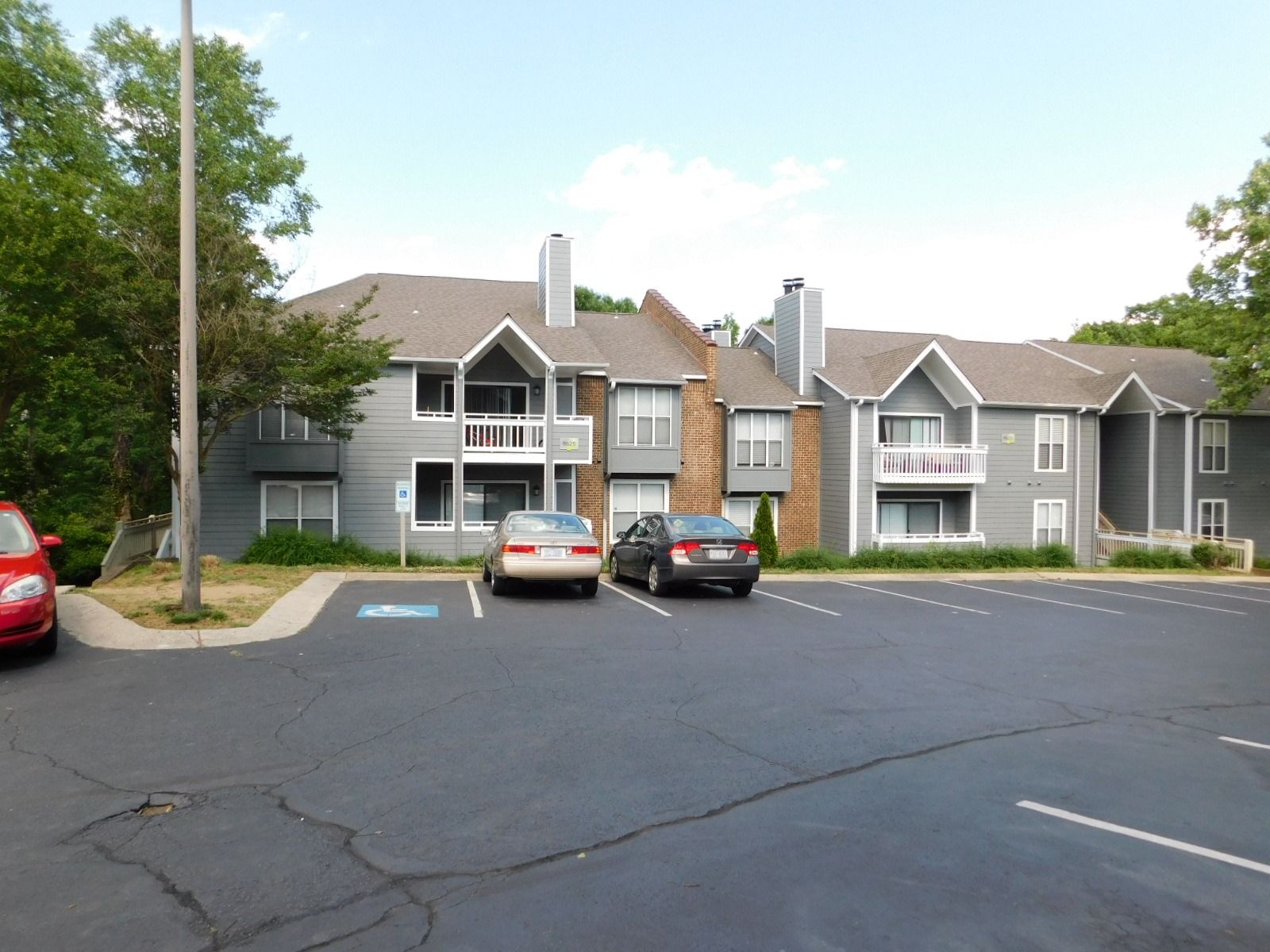 Apartment building with parked cars in front and a mostly empty parking lot