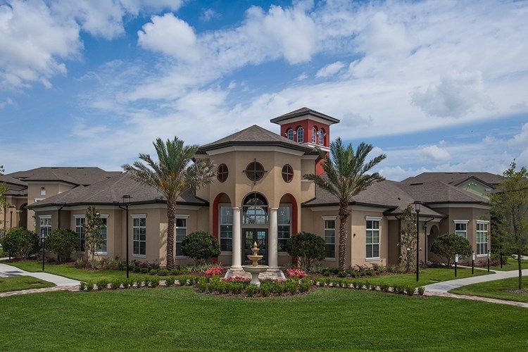 Large Mediterranean-style building with arched columns, red tower, and manicured lawn under a cloudy sky