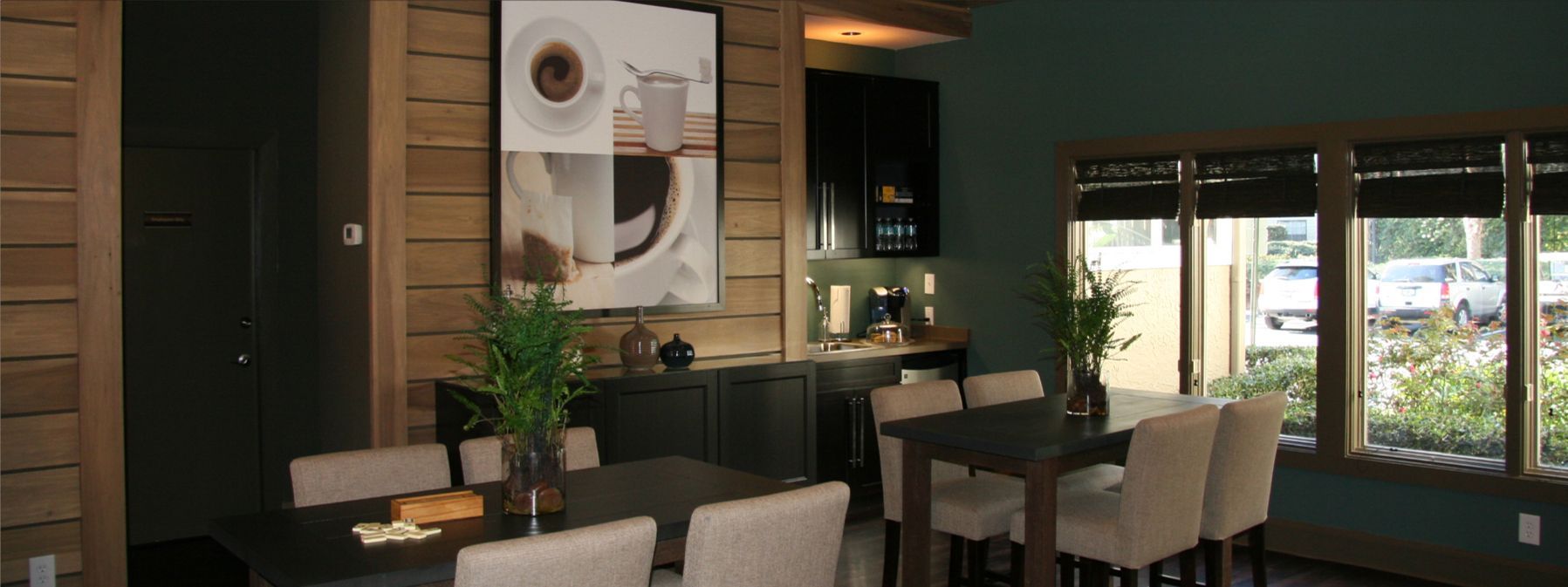 Modern dining room with long table, white chairs, wall art, and large windows overlooking greenery