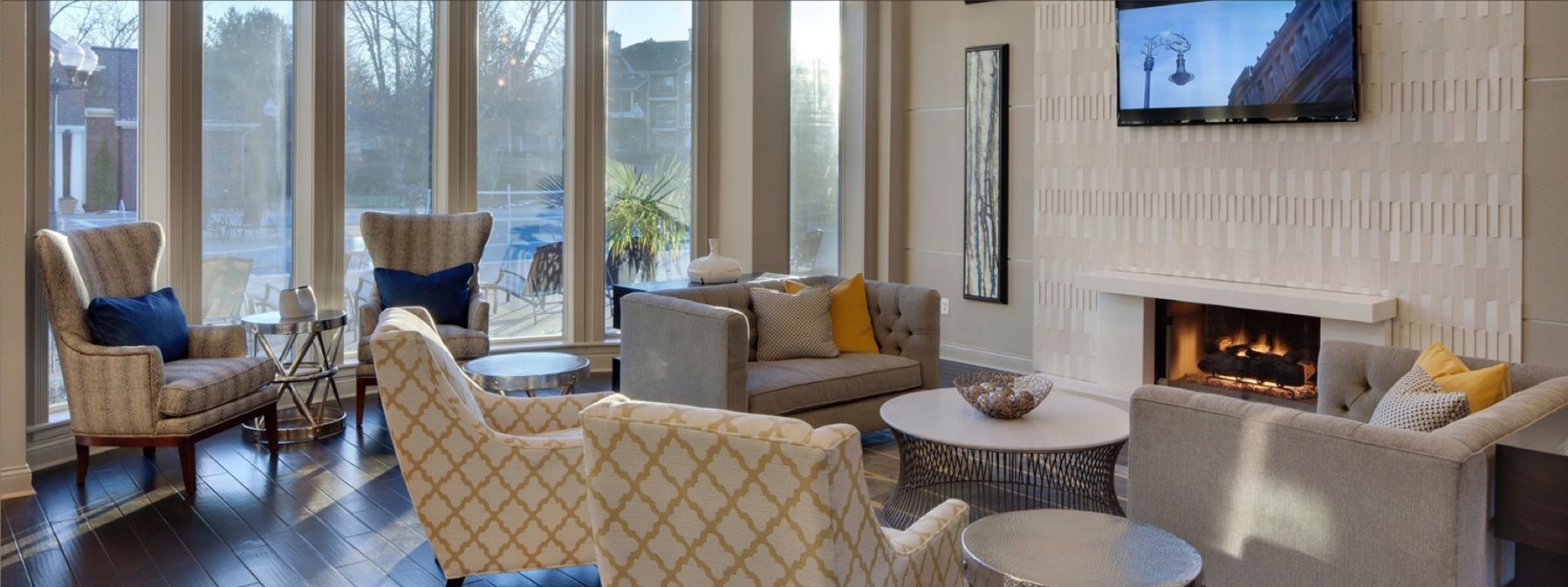 Modern living room with chairs, sofas, fireplace, and large windows overlooking trees