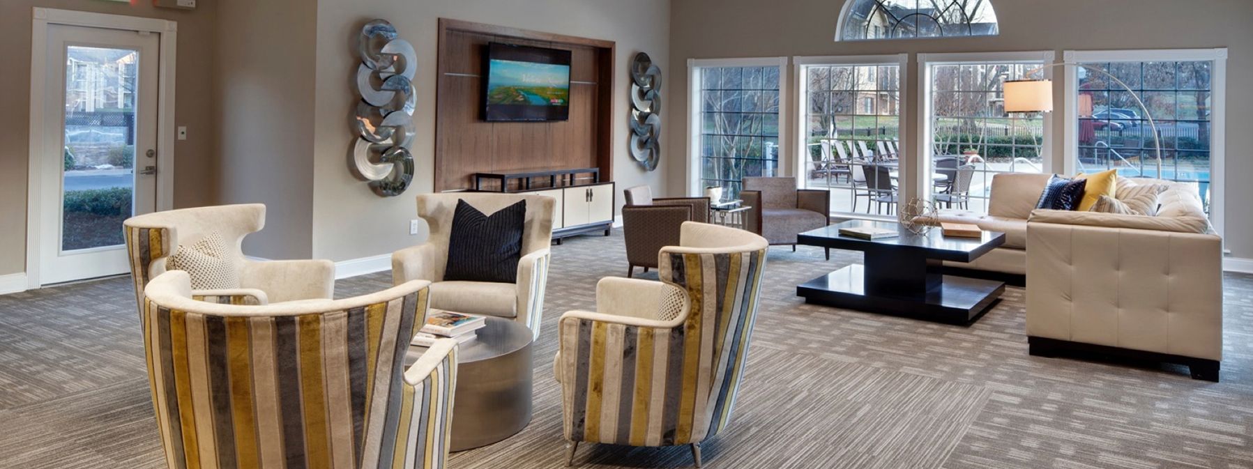 Modern living room with striped chairs, beige sofa, wall-mounted TV, and large windows overlooking a snowy view