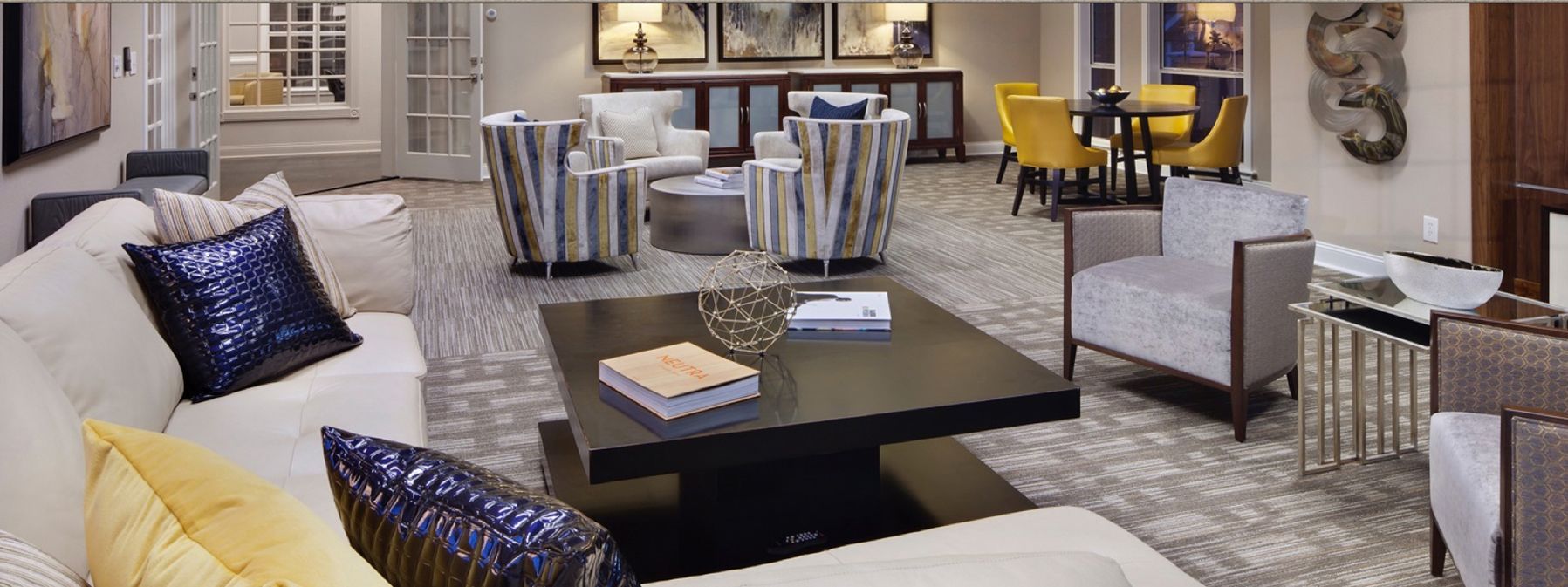 Modern living room with white sectional, black coffee tables, patterned chairs, and yellow accent pillows