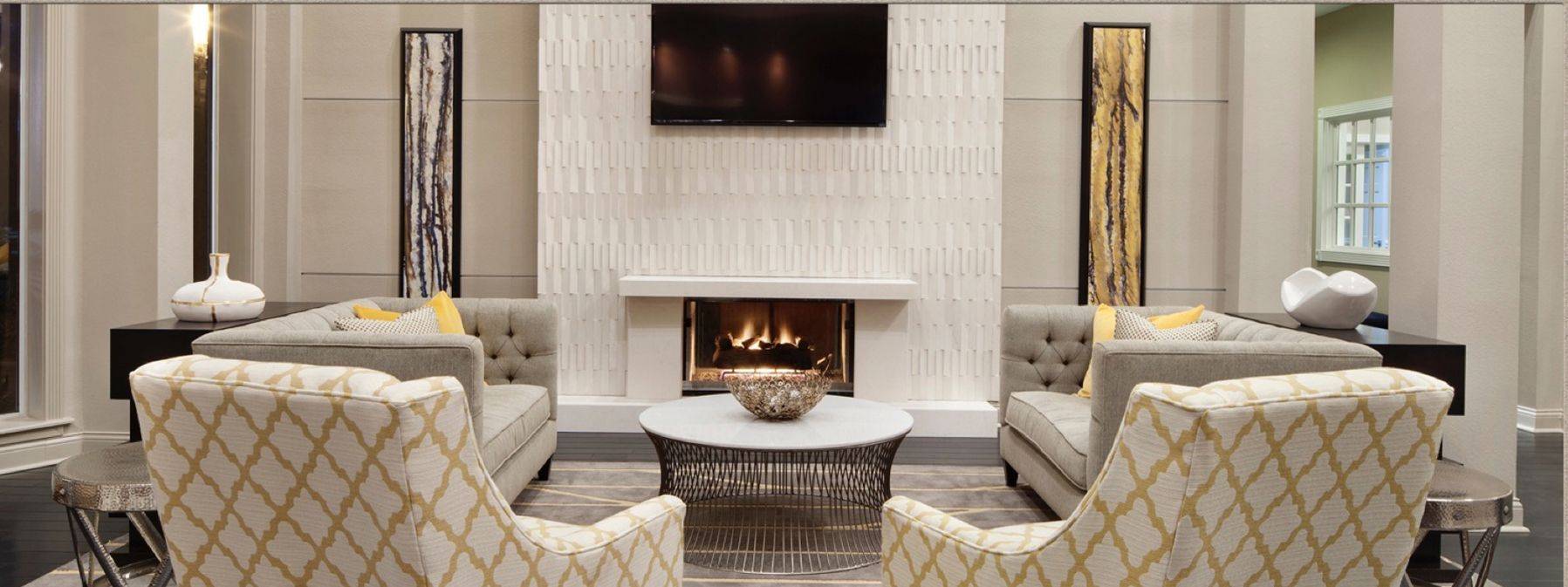 Elegant living room with a white fireplace, wall-mounted TV, and two patterned armchairs facing a round coffee table.