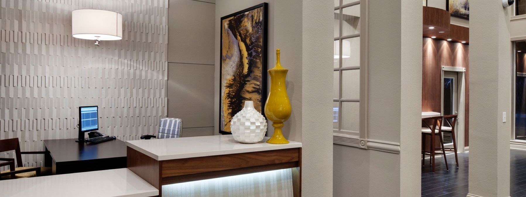 Modern office reception area with desk, chair, wall art, and yellow vase beside an open doorway