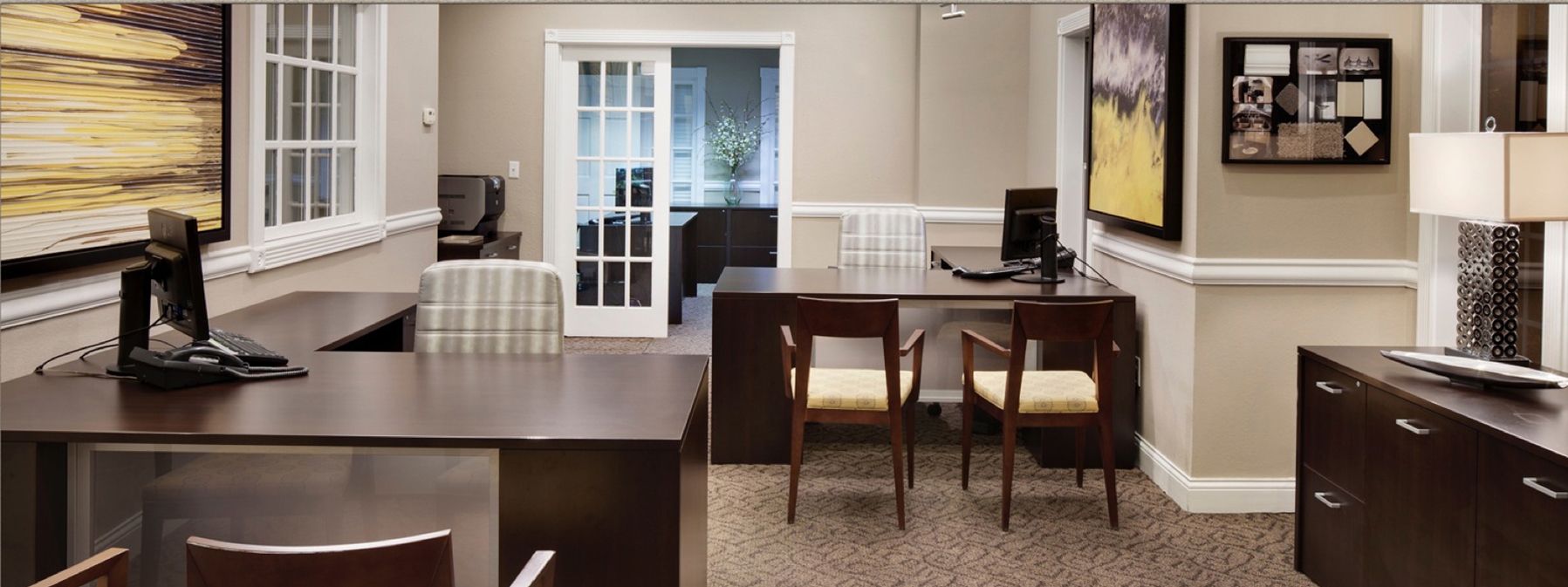 Modern kitchen with dark island, two stools, white cabinets, and a small desk area near sliding glass doors