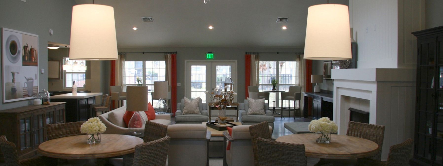 Bright hotel lobby with sofas, armchairs, round tables, and hanging lamps around a central fireplace.