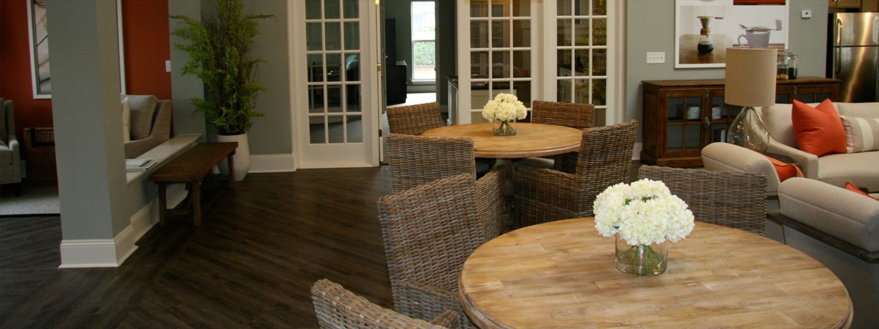 Cozy living room with wicker chairs, round wooden tables, white flowers, and French doors to a patio