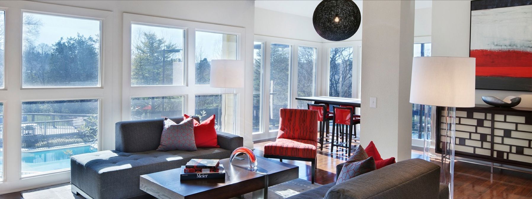 Modern living room with large windows, gray sofa, red chairs, floor lamp, and snowy view outside