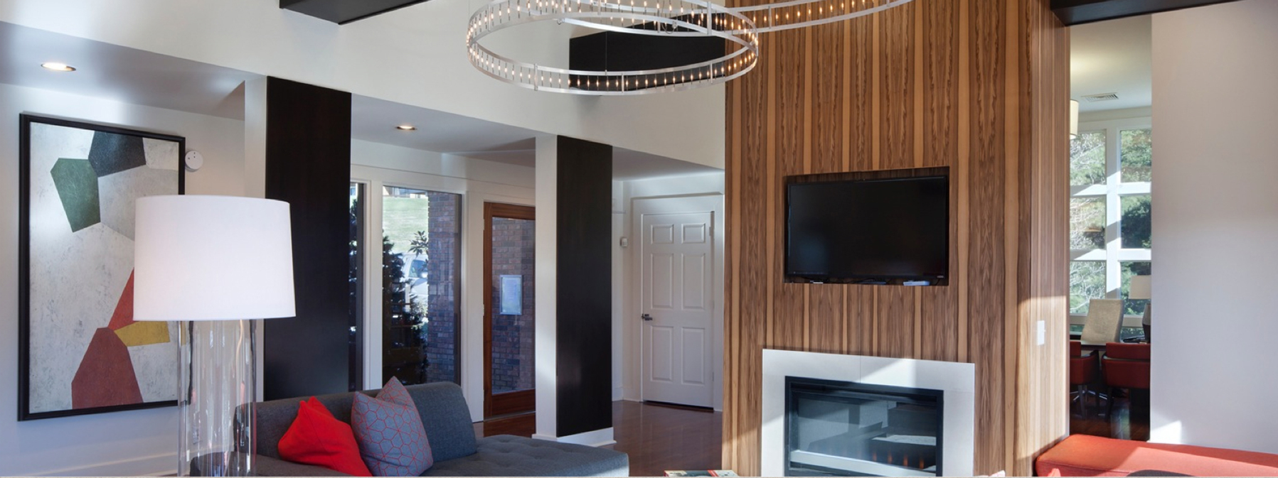 Modern living room with fireplace, wall-mounted TV, white lamp, and red-accented seating