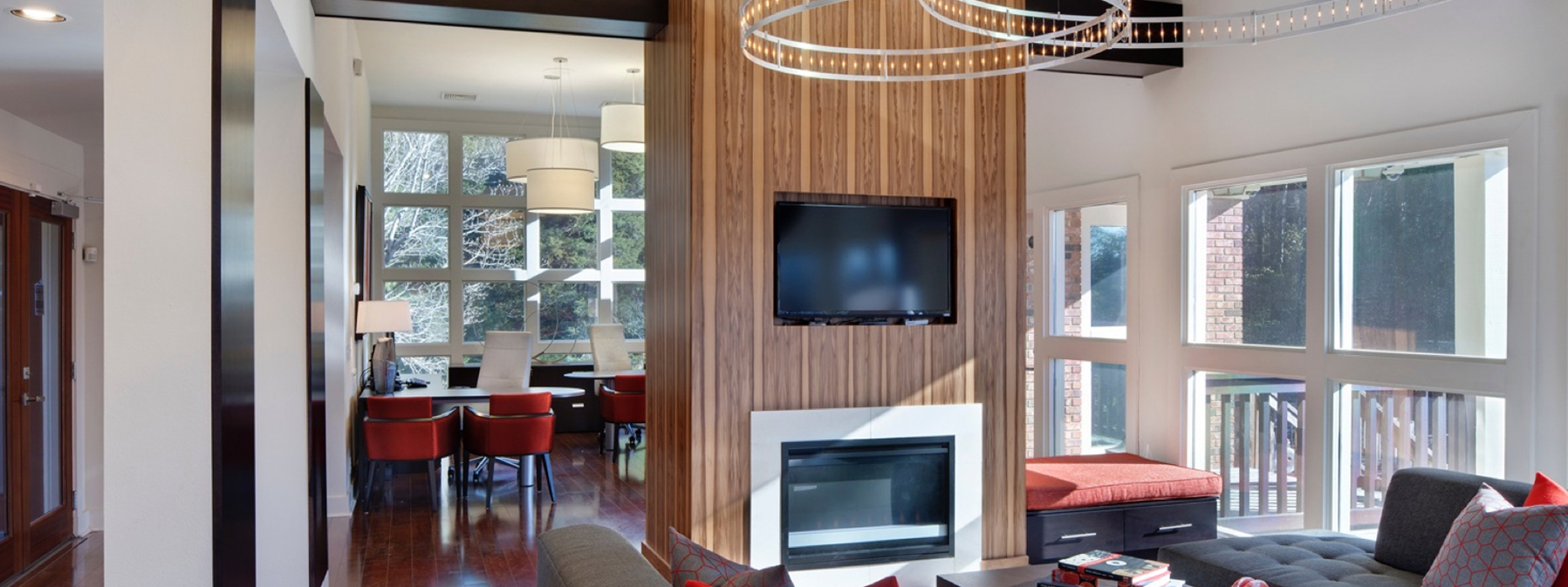 Bright modern living room with fireplace, wall-mounted TV, and large windows overlooking a dining area