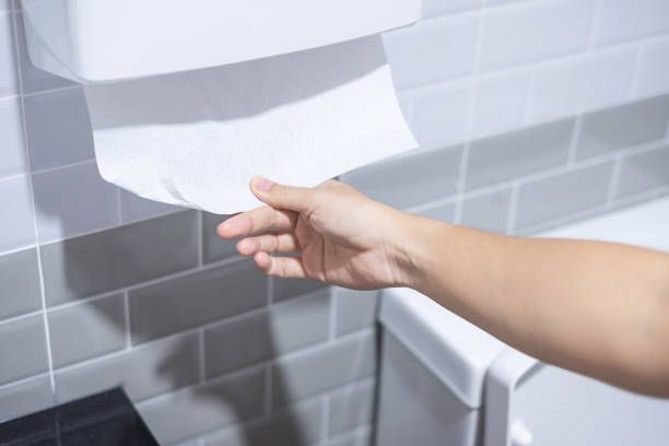 Una persona saca un rollo de papel higiénico de un dispensador en un baño.
