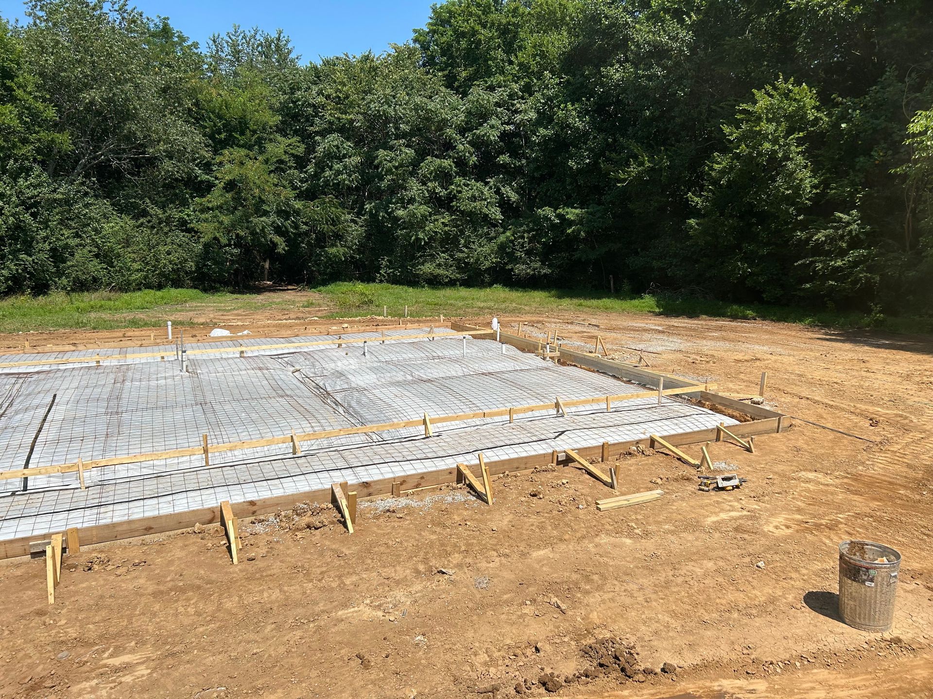 A concrete foundation is being built in a dirt field with trees in the background.