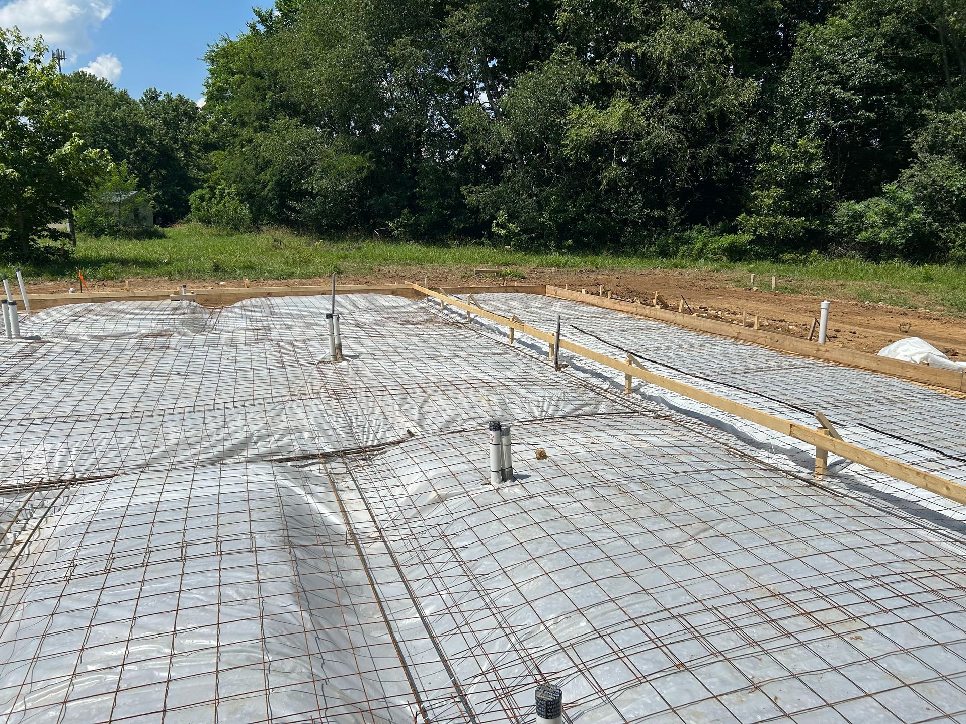 A concrete foundation is being built in a field with trees in the background.