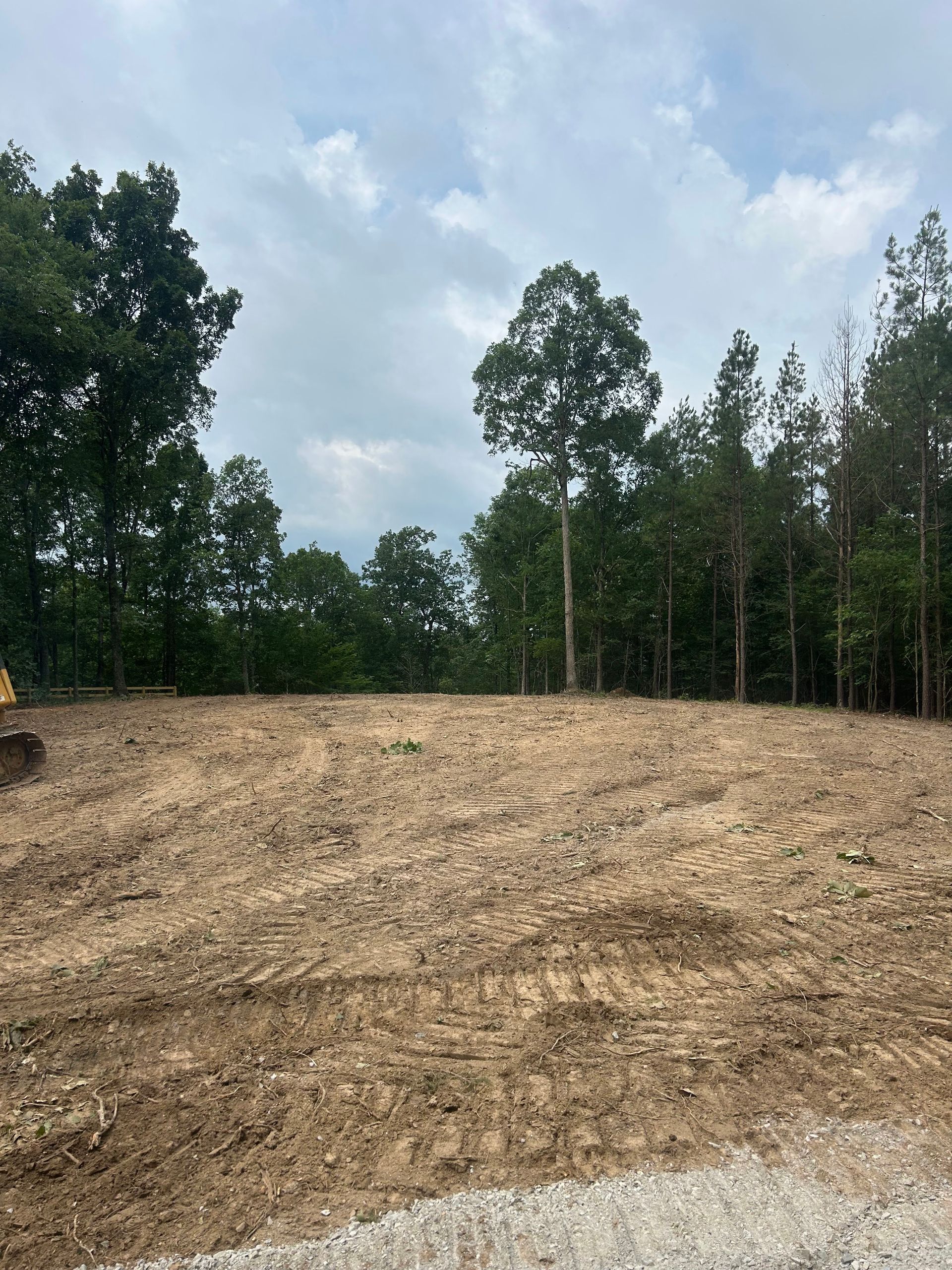 A large dirt field with trees in the background and a bulldozer in the foreground.