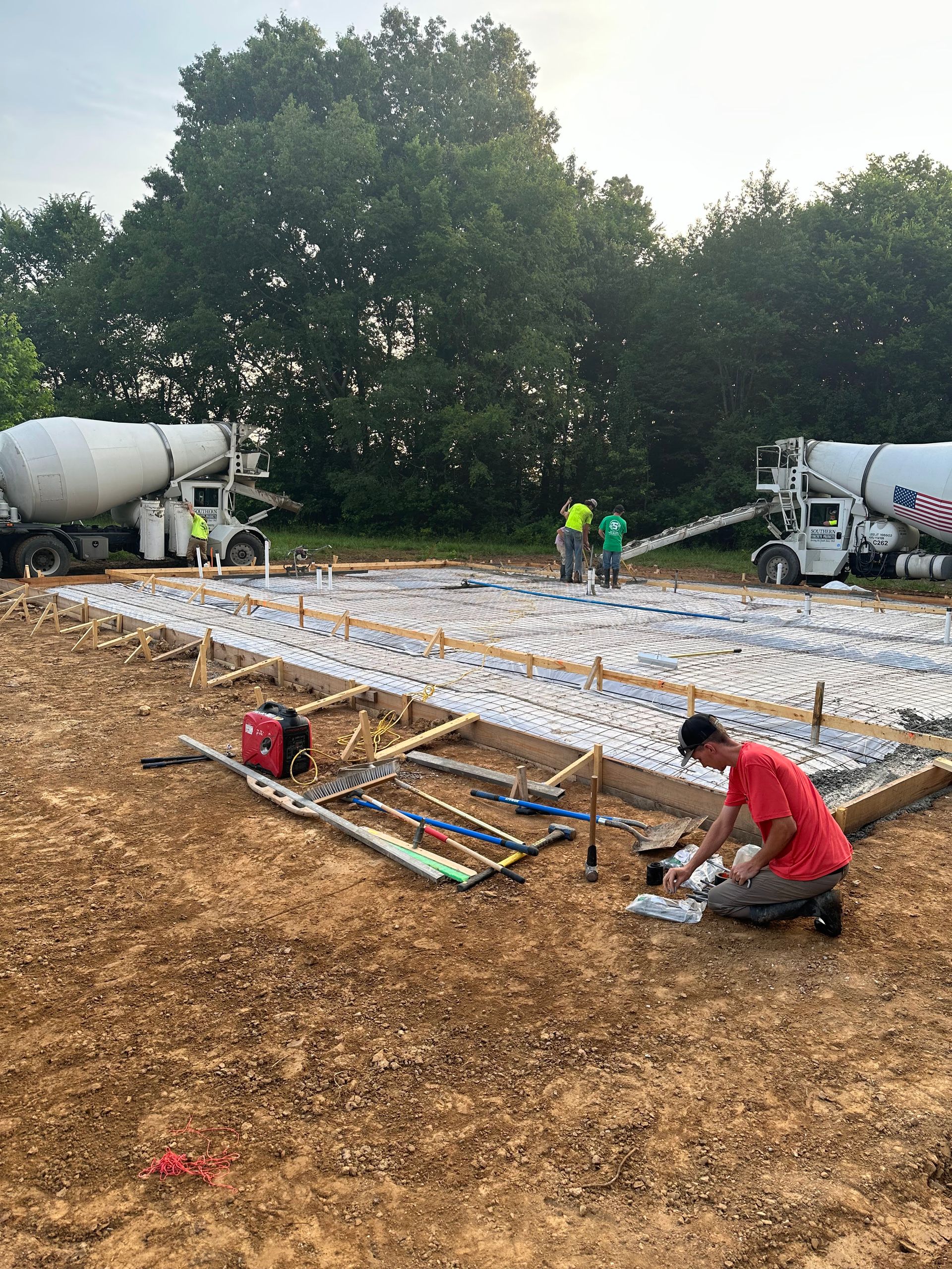 A man is kneeling in the dirt in front of a concrete mixer truck.