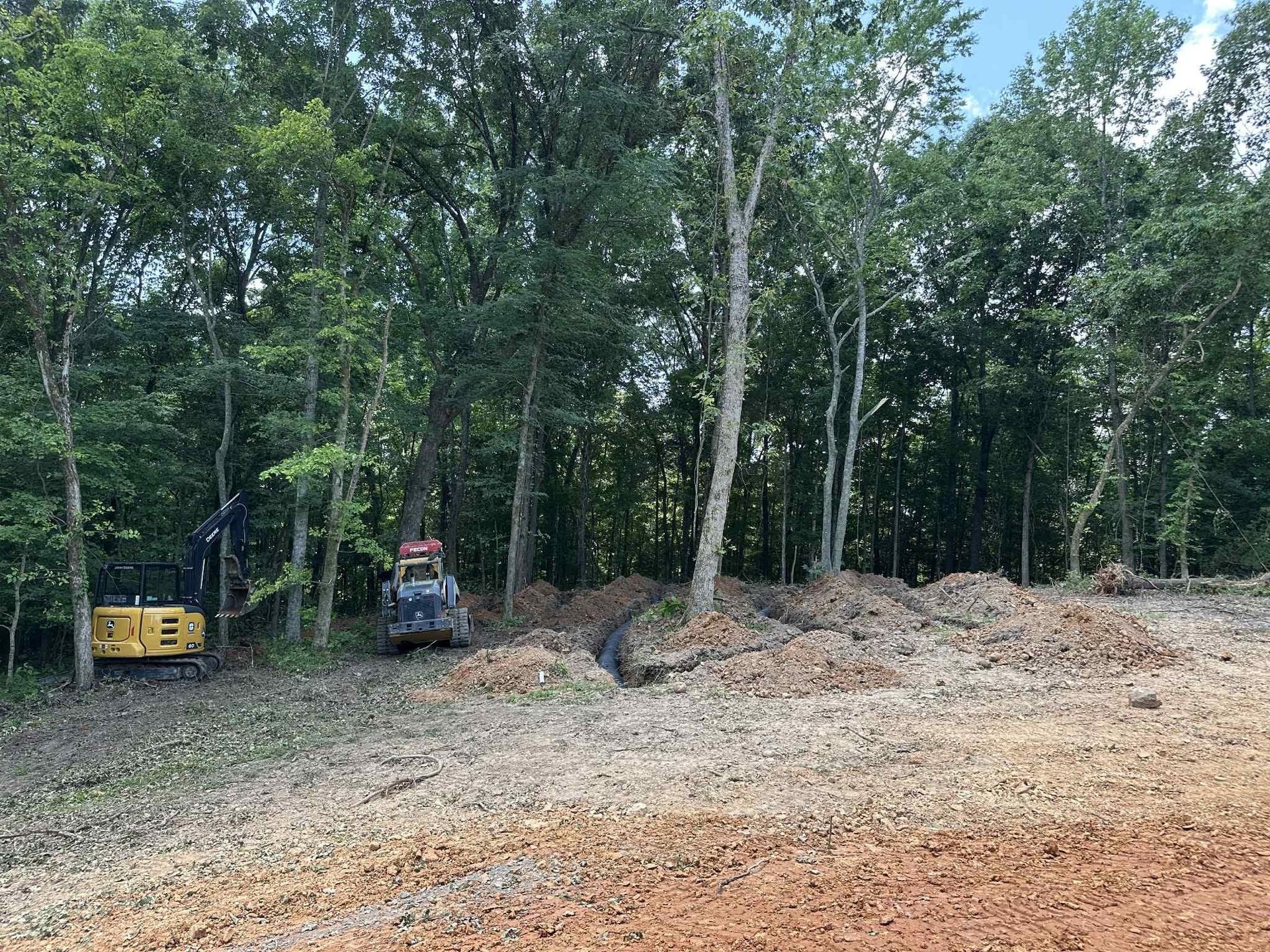 A bulldozer is sitting in the middle of a dirt field surrounded by trees.