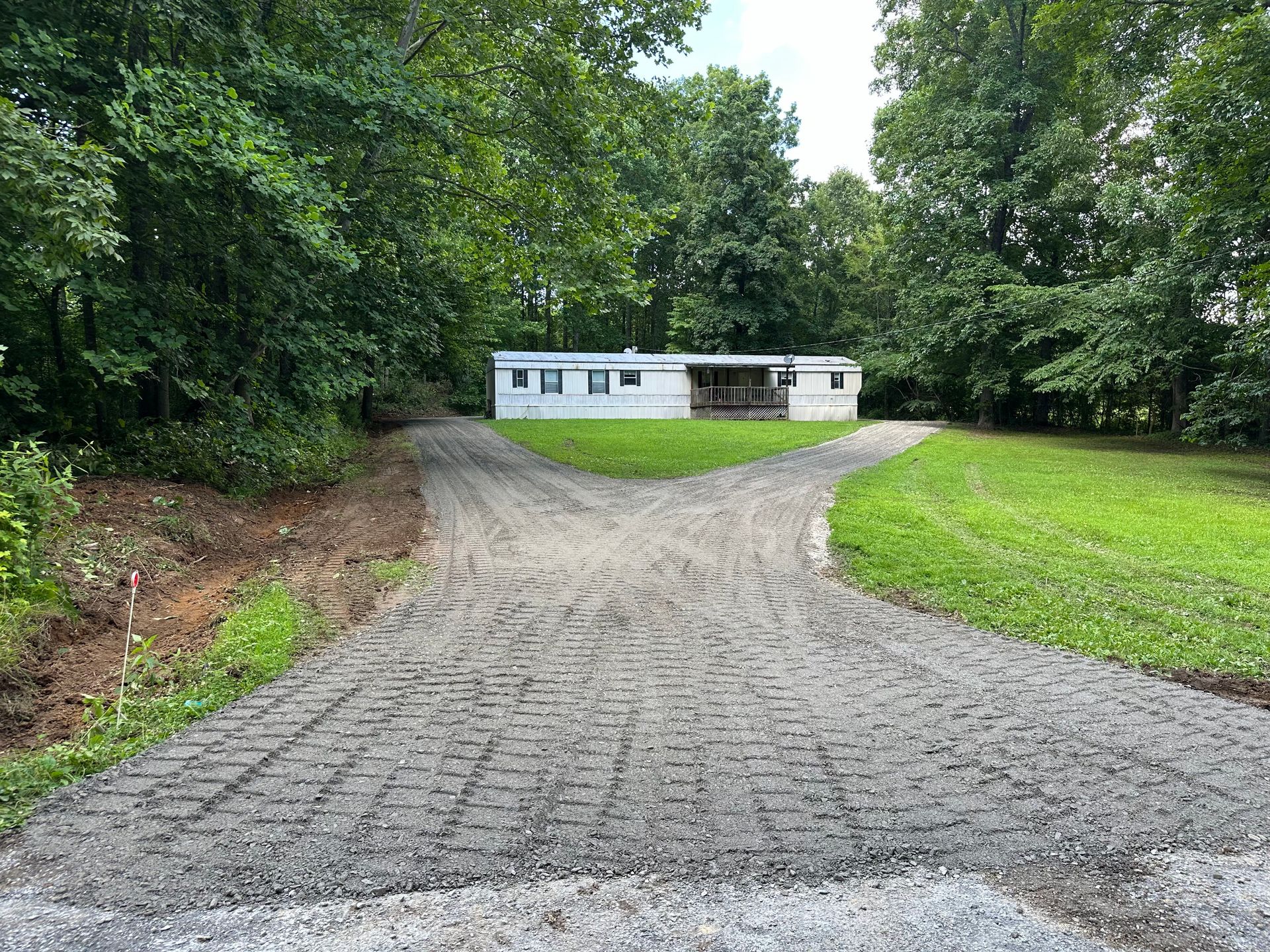 A dirt road leading to a mobile home surrounded by trees.