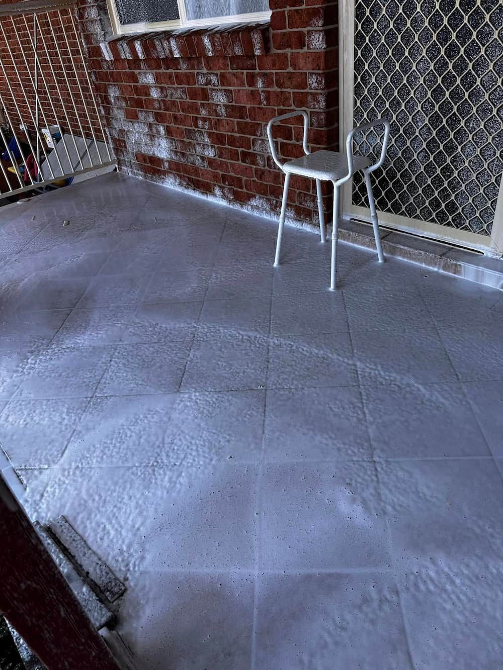 A White Chair is Sitting on a Tiled Floor Next to a Brick Wall — Lighthouse pressure washing in Lake Cathie, NSW