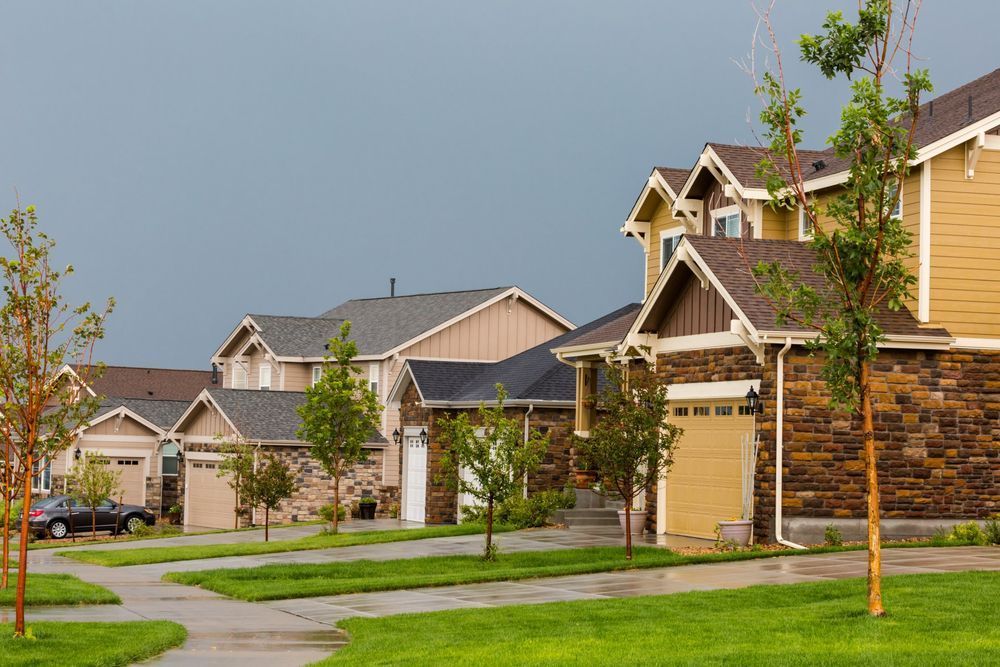 Row of suburban houses with garages and green lawns under a cloudy sky.